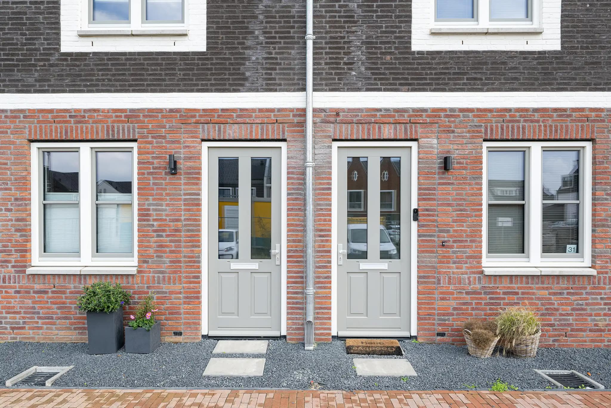 Twee lichtgrijze klassieke paneeldeuren met glas in een gevel van rode baksteen