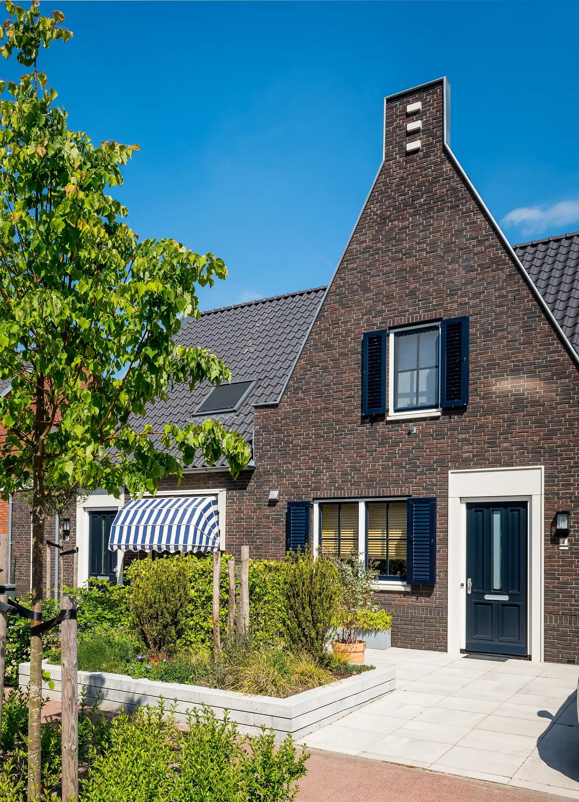 Donkere bakstenen woning met puntgevel en een strakke donkerblauwe voordeur