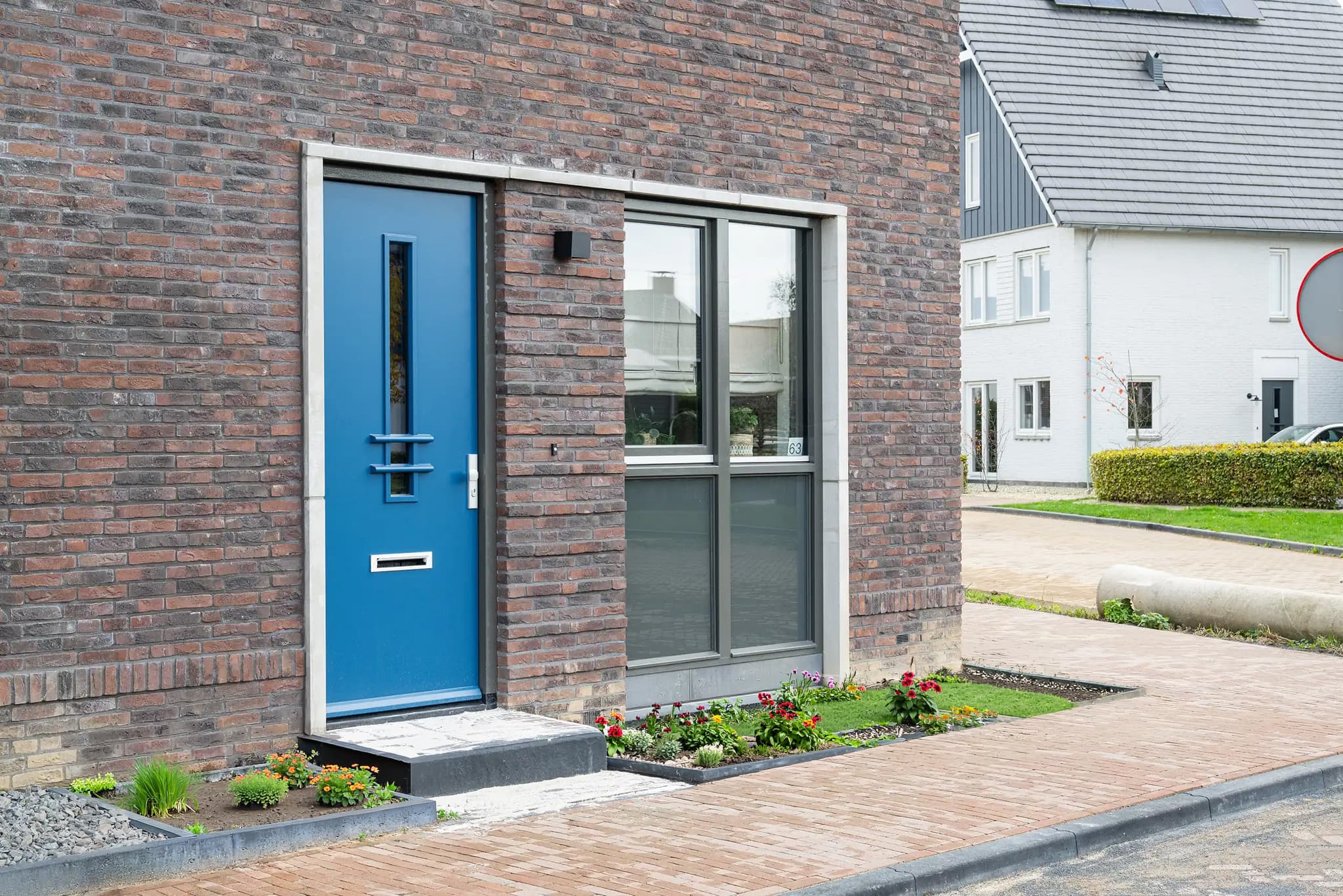 Helderblauwe voordeur met smal verticaal glaspaneel in een donkere bakstenen gevel